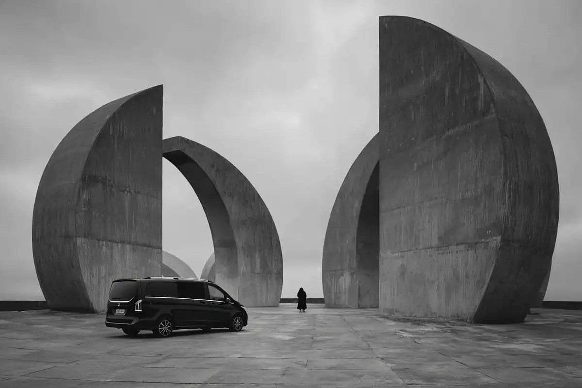 Brutalist concrete plaza under heavy cloud with a black van in a minimal composition.