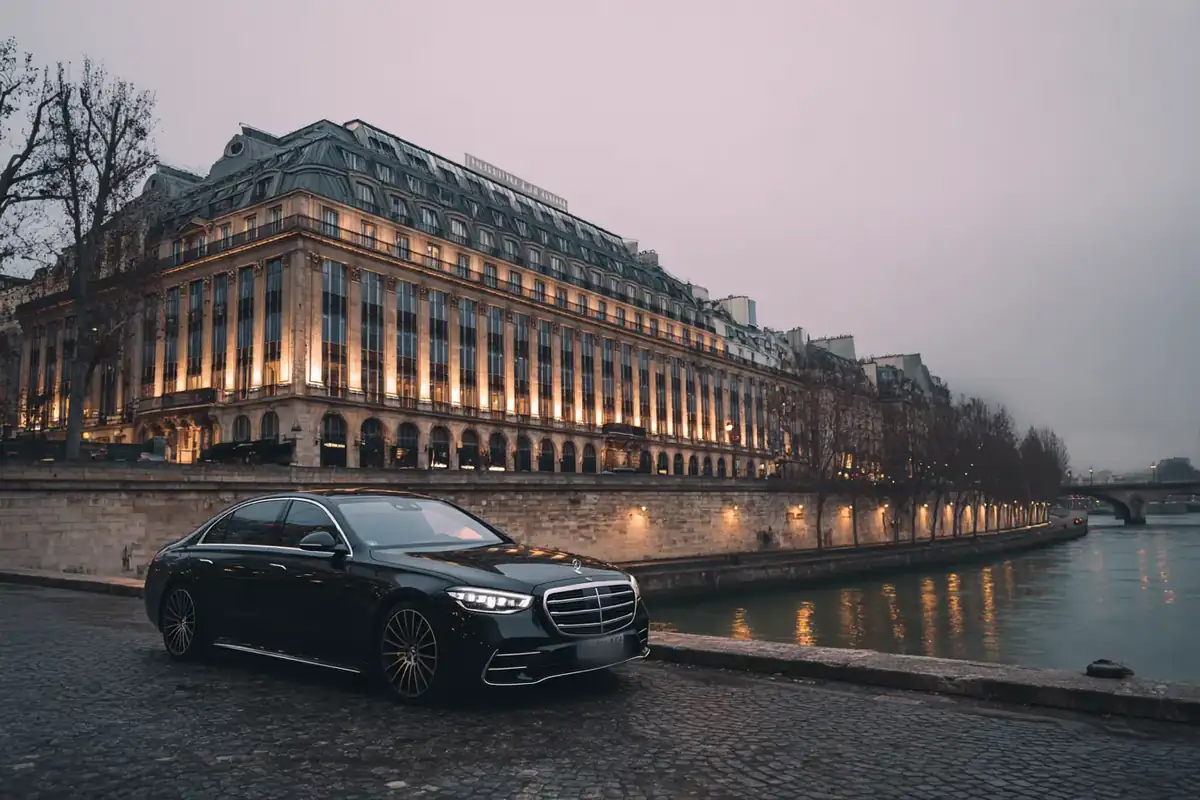 Black sedan on a Seine quay before a grand Art Deco building at dawn.
