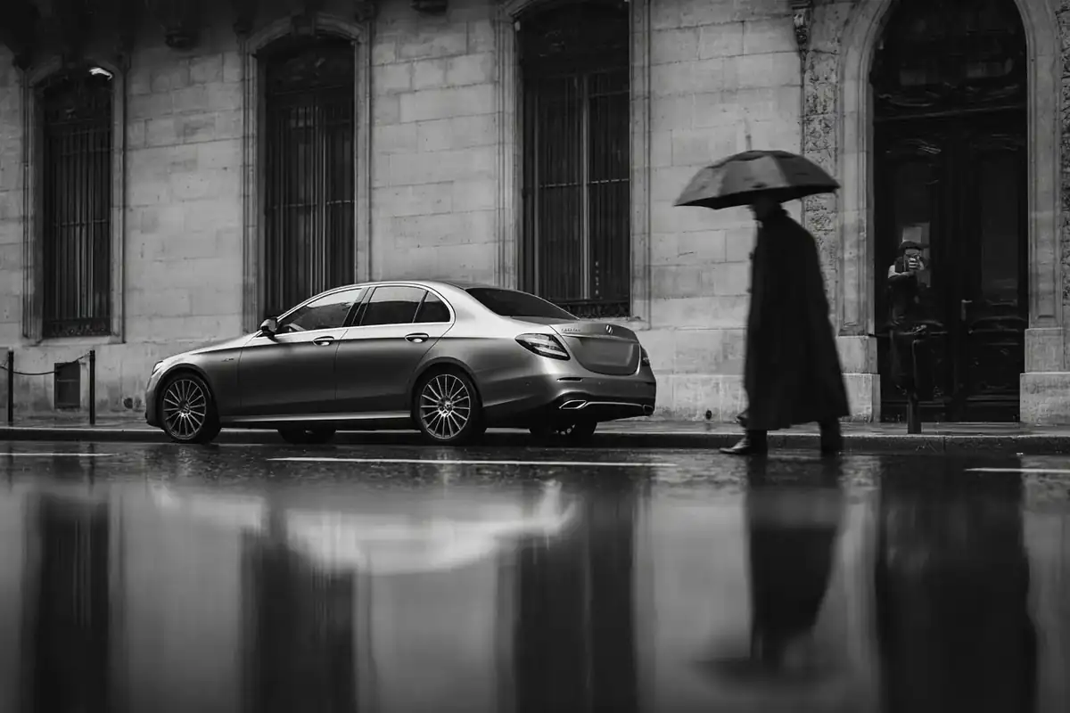 Rain-soaked monochrome Paris street with a black sedan reflected in puddles.