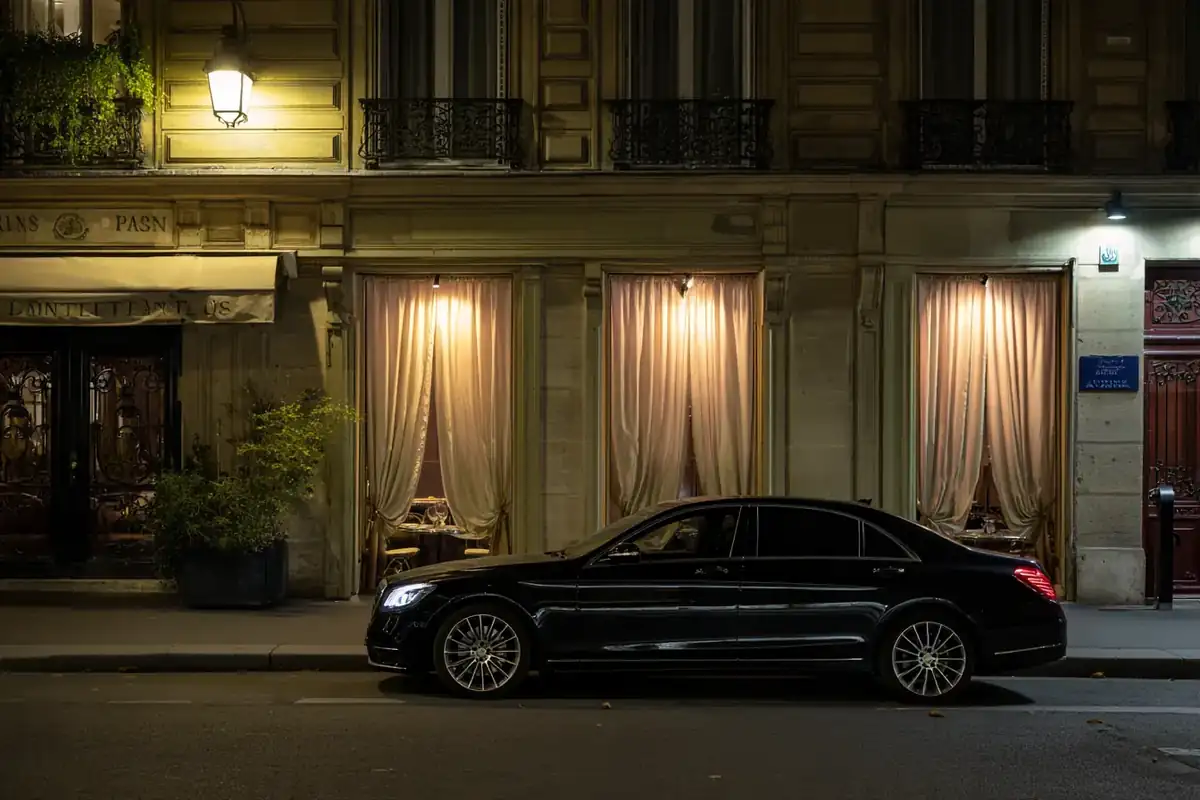 Black sedan on a Haussmann street at night beside a softly lit restaurant.
