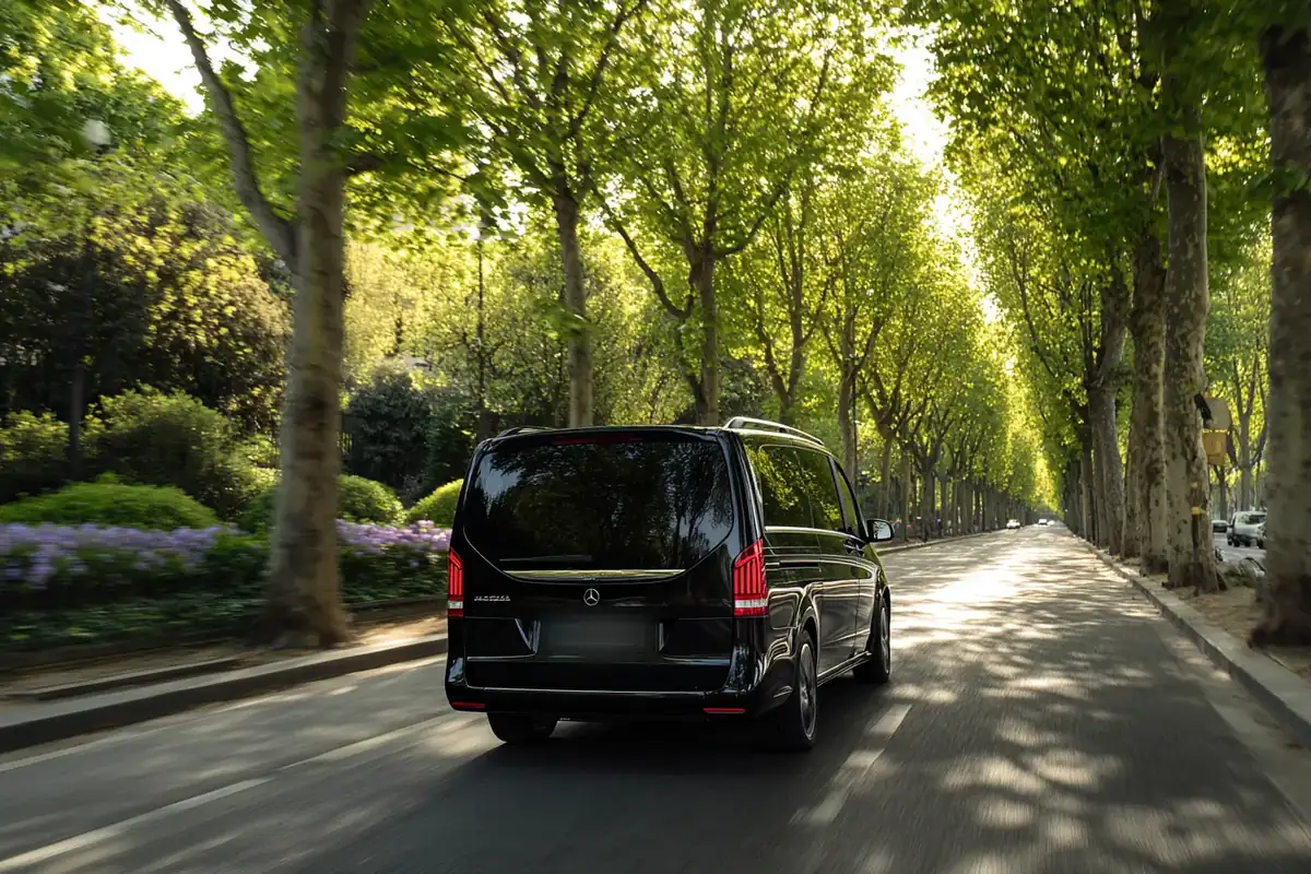 Black van on a tree-lined road toward the Bois de Boulogne in spring.