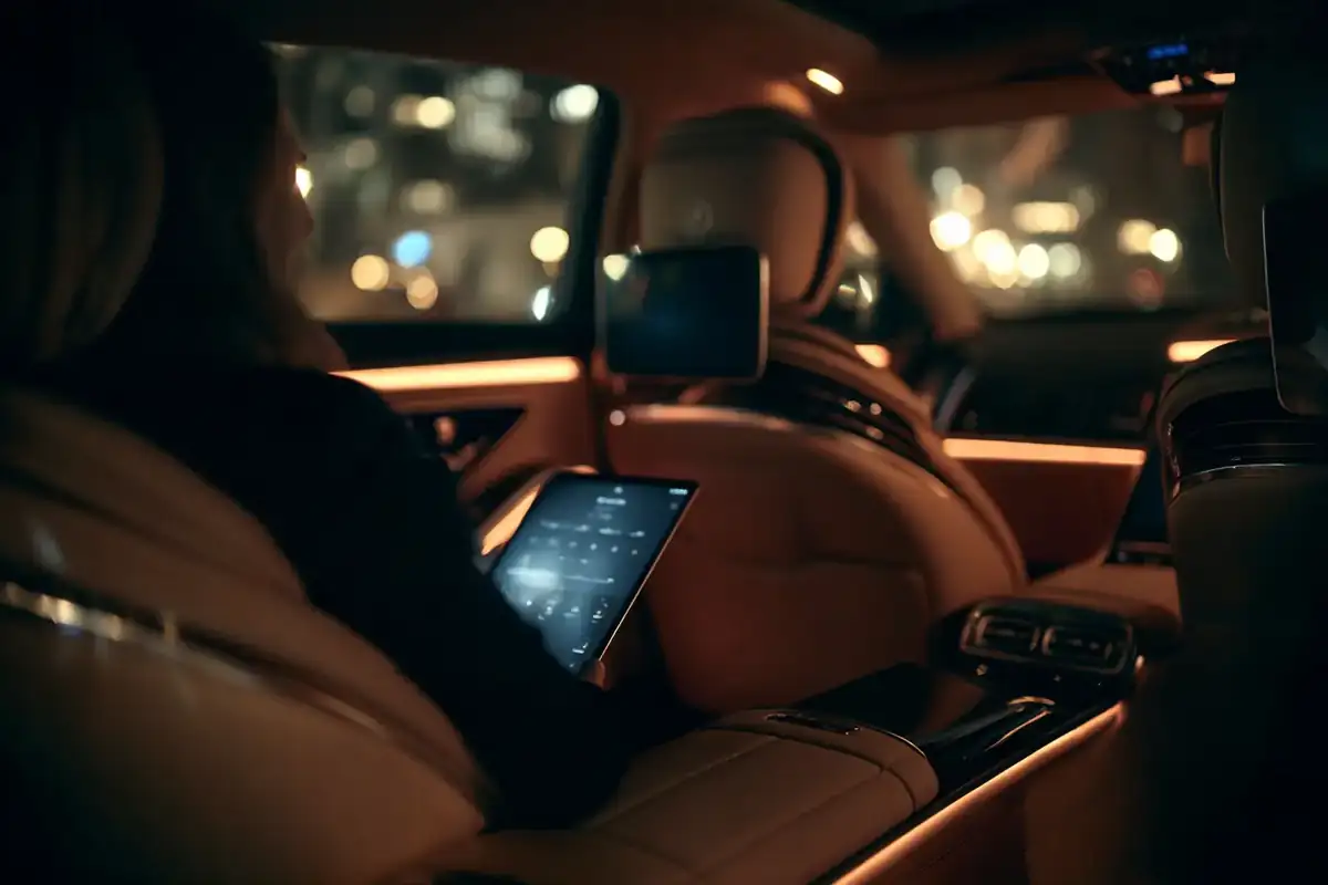 Rear cabin of a black sedan at night, an executive assistant reviewing a tablet.