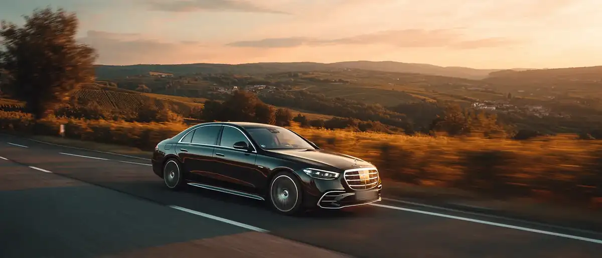 Black sedan alone on a French motorway at golden hour with vineyards on both sides.
