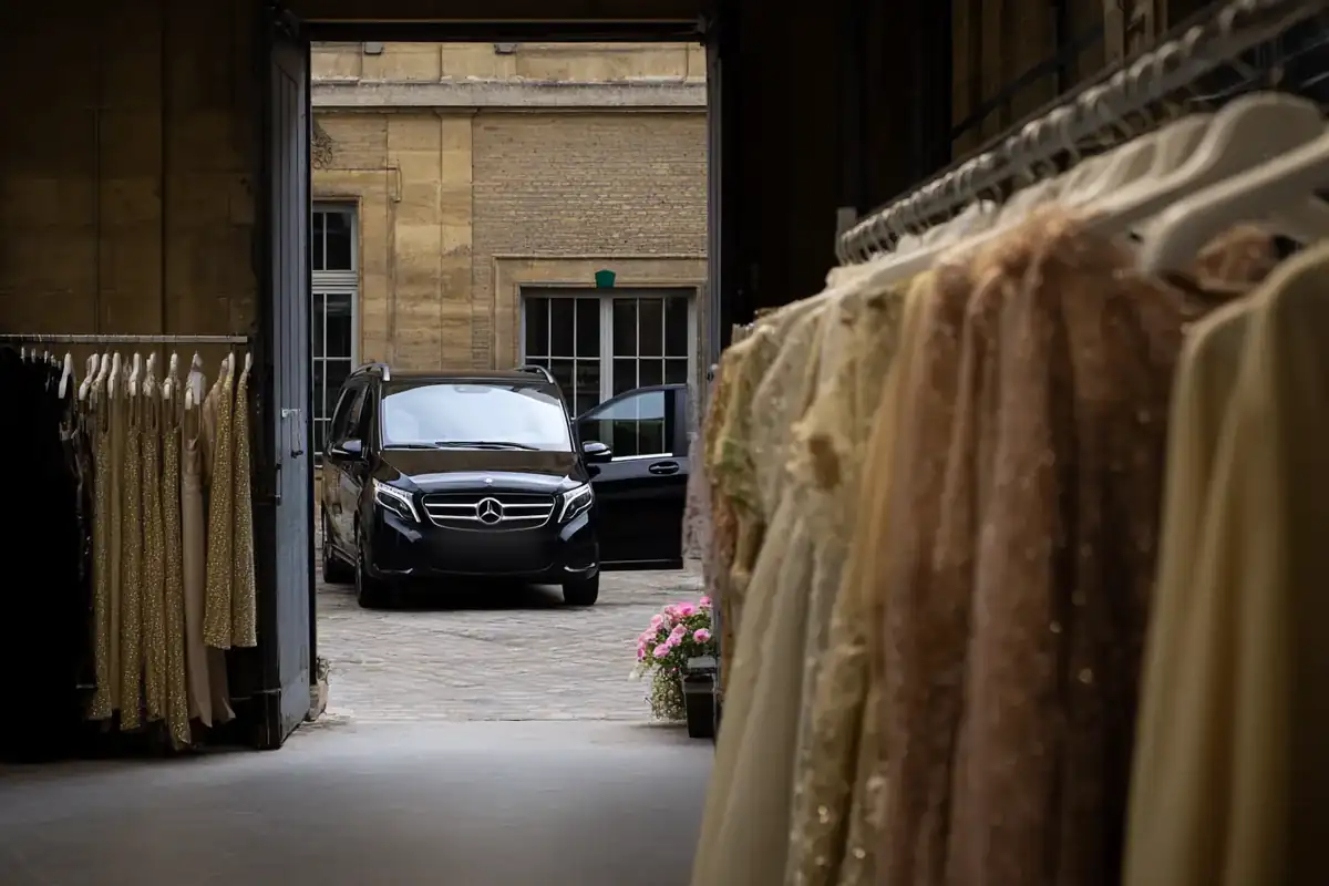 Backstage garment racks with a black van waiting in a stone courtyard.