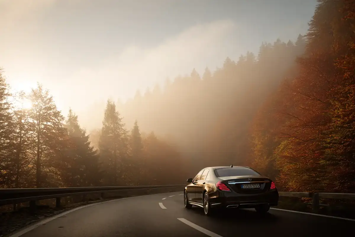 Black sedan on a misty autumn forest road in the Jura mountains.