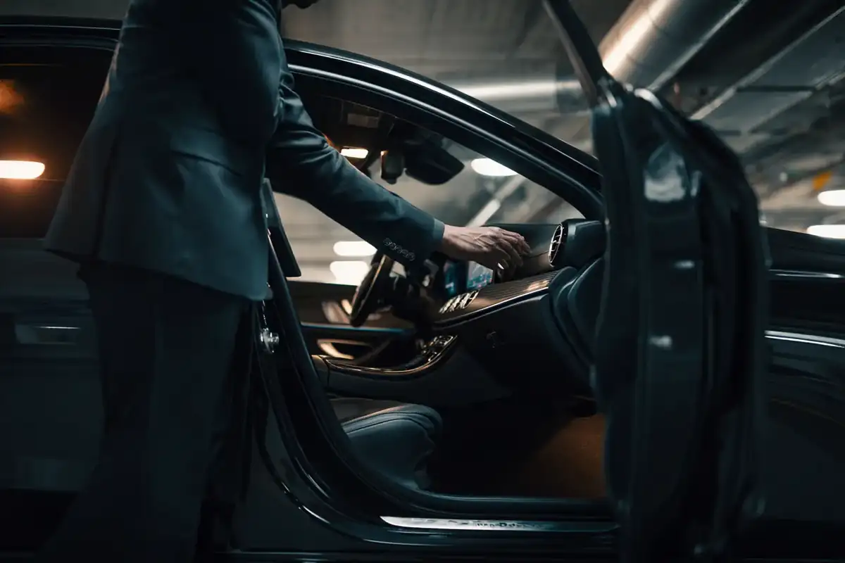 Chauffeur in a dark suit performing a pre-service check of a Mercedes interior in a garage.
